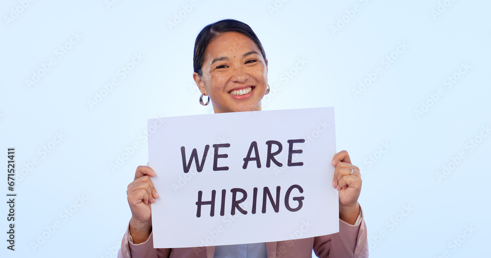 Recruitment, smile and portrait of woman in a studio with a hiring sign, poster or board for job. Happy, employment and face of young Asian female person advertising a career offer by blue background Recruitment, smile and portrait of woman in a studio with a hiring sign, poster or board for job. Happy, employment and face of young Asian female person advertising a career offer by blue background