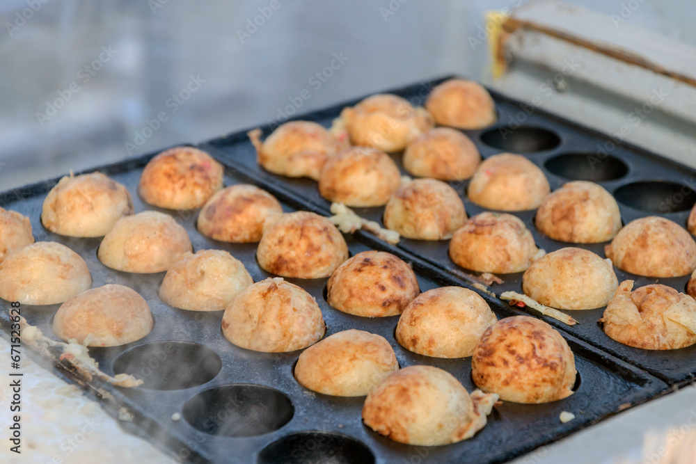 Cooking Takoyaki made of a wheat flour-based and cooked in a special moulded in a shape of little round balls containing pieces of octopus. Famous street food in Japan. Cooking Takoyaki made of a wheat flour-based and cooked in a special moulded in a shape of little round balls containing pieces of octopus. Famous street food in Japan.