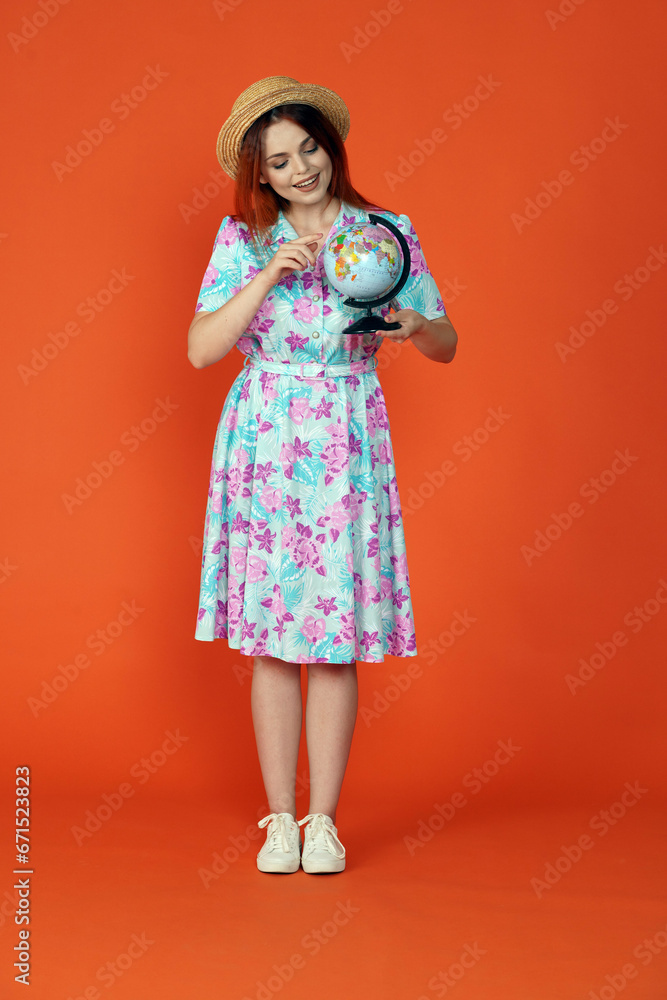 Woman holding small globe, smiling looking and pointing at the map picking destination, isolated on orange background. Portrait of female traveler. Woman holding small globe, smiling looking and pointing at the map picking destination, isolated on orange background. Portrait of female traveler.