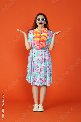 Woman in glasses and flower wreath standing posing with surprised face holding open hands up, isolated on orange background. Portrait of female traveler.
