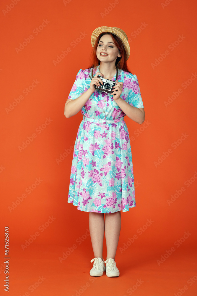 Woman standing holding old film camera, looking at the attractions around and smiling, isolated on orange background. Portrait of female traveler. Woman standing holding old film camera, looking at the attractions around and smiling, isolated on orange background. Portrait of female traveler.