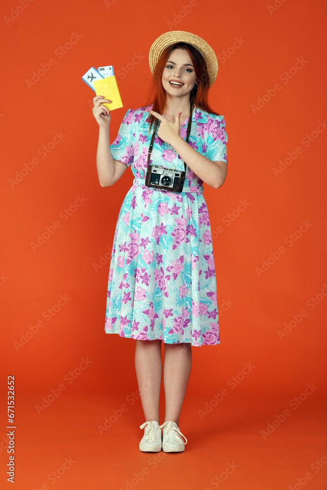 Woman standing holding flight tickets and passport, pointing at it and smiling at the camera, isolated on orange background. Portrait of female traveler. Woman standing holding flight tickets and passport, pointing at it and smiling at the camera, isolated on orange background. Portrait of female traveler.
