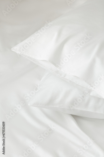 Two white pillows in satin or silk or lyocell pillowcases on white sheet. Bedding and accessories. Home textile photo