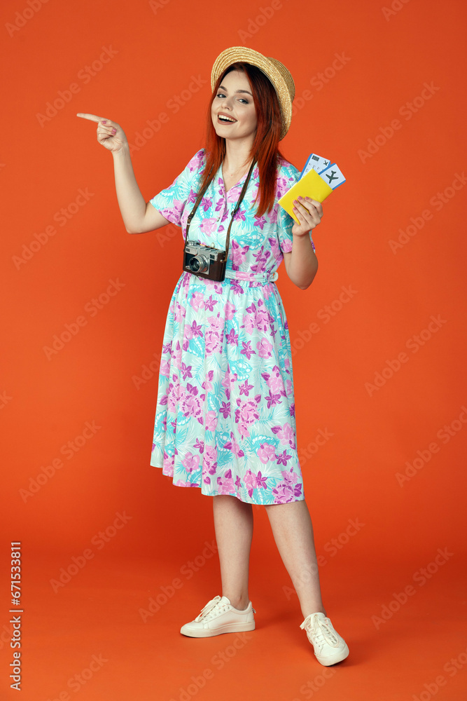 Woman with flight tickets looking at the camera pointing at the empty area for advertisement, isolated on orange background. Portrait of female traveler.