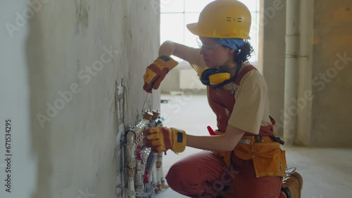 Female plumber screwing pipes to wall at construction site