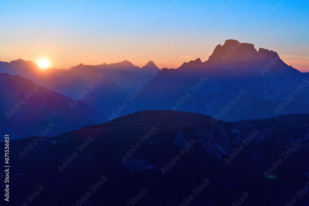 View of the Dolomites panorama with the setting sun in the dark blue evening sky. Shades of orange, dark blue to purple. A moment of calm, a sense of space. Autumn on a hike in the Dolomites, Italy.