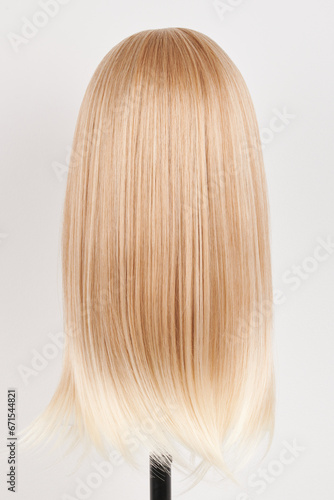 Natural looking blonde wig on white mannequin head. Long hair on the plastic wig holder isolated on white background, back view.