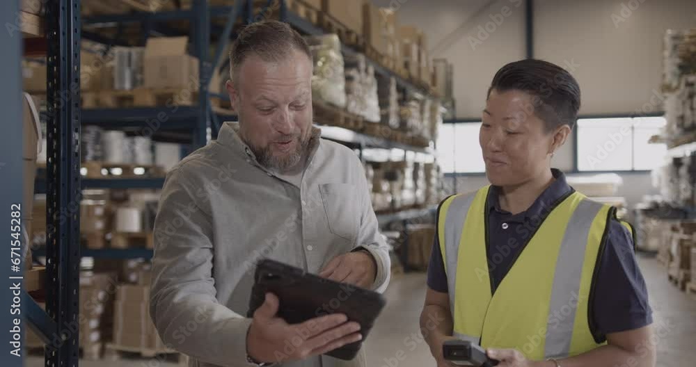 Two Warehouse Employees Looking at Digital Tablet Discussing Inventory Two Warehouse Employees Looking at Digital Tablet Discussing Inventory