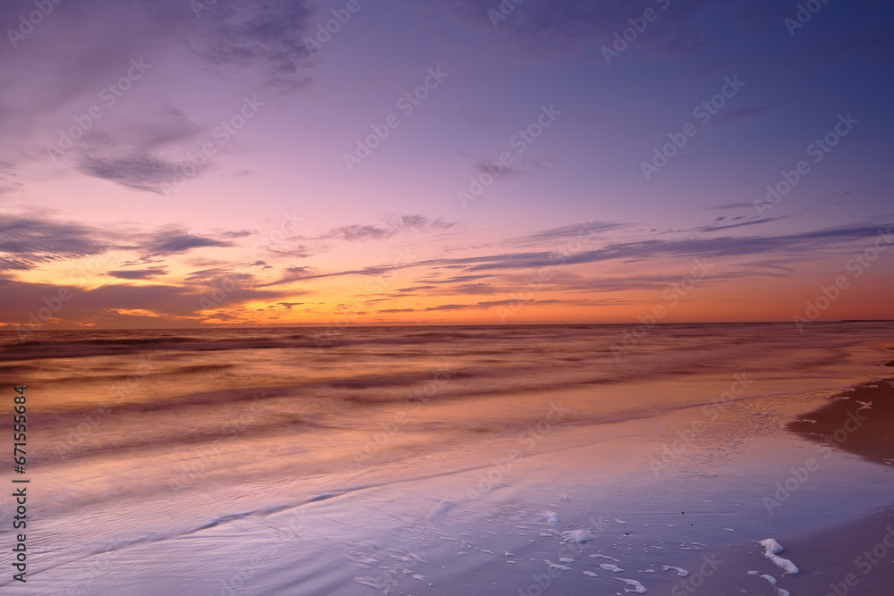 Seascape and landscape of a beautiful sunset on the west coast of Jutland in Loekken, Denmark. Sun setting on the horizon on an empty beach at dusk over the ocean and sea in the evening