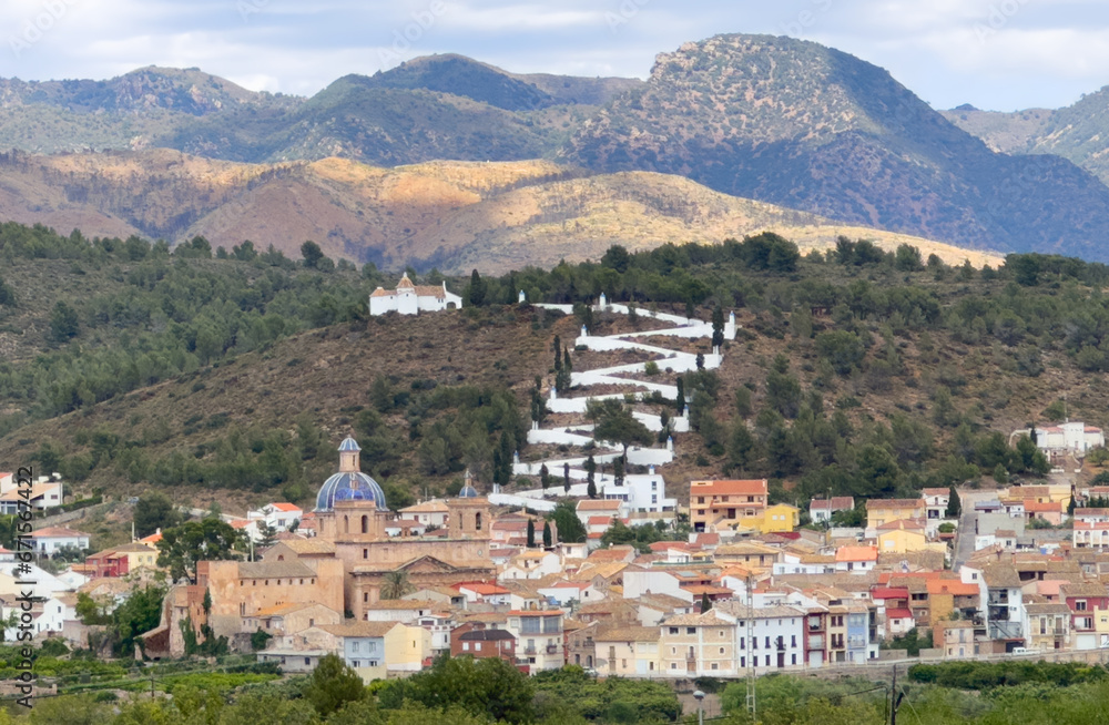 Naklejka premium Sot de Ferrer town, Valencia, Spain. Rural landscape. Buildings and houses in city. Town at mountain. Town at Mountains hills. Houses roofs in countryside. Orange Mandarin trees at farm field.