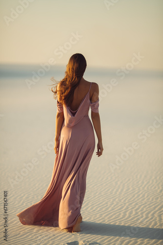 Walking romantic fashionable woman model in the desert in evening pink dress.Back view of gorgeous slim girl outdoor epic high quality photo