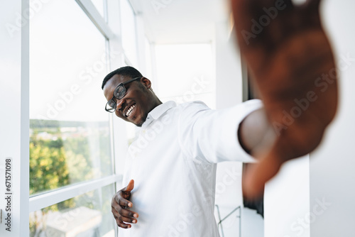 Young african man in white shirt and glasses posing near large window