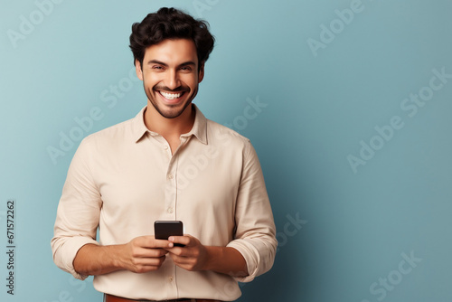 Portrait of cheerful handsome entrepreneur with hand in pocket messaging online over smart phone. Happy young man dressed in blue jeans shirt posing confidently