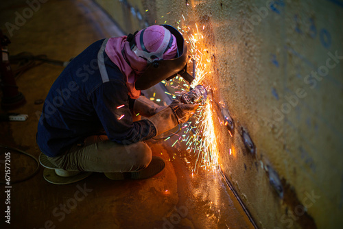 Worker using electric wheel spark grinding on welder metal carbon steel part shell plate inside tank photo