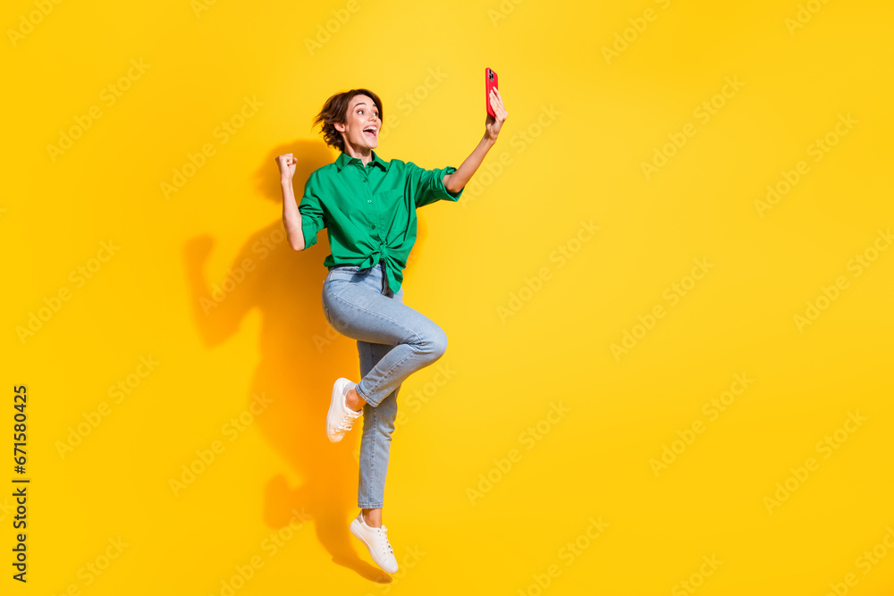 Full length photo of lucky impressed lady wear green shirt jumping high recording video vlog empty space isolated yellow color background