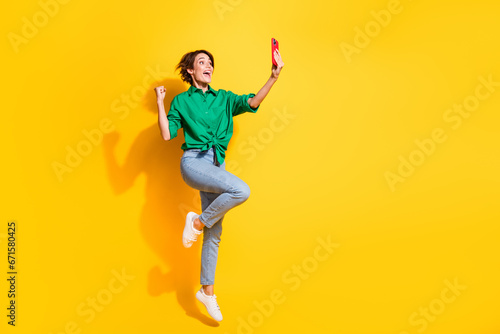 Full length photo of lucky impressed lady wear green shirt jumping high recording video vlog empty space isolated yellow color background
