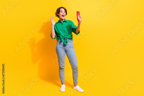 Full length photo of cute excited lady wear green shirt waving arm recording video vlog empty space isolated yellow color background © deagreez