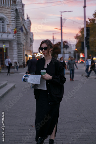 Stylish girl with newspaper walking in city at the evening. © Corina