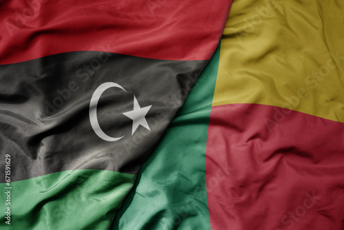 big waving national colorful flag of libya and national flag of benin .