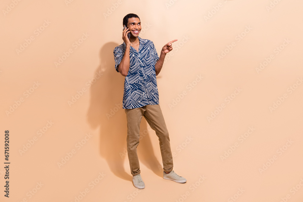 Full length photo of cheerful man dressed shirt directing look at promo empty space talk on smartphone isolated on beige color background Full length photo of cheerful man dressed shirt directing look at promo empty space talk on smartphone isolated on beige color background