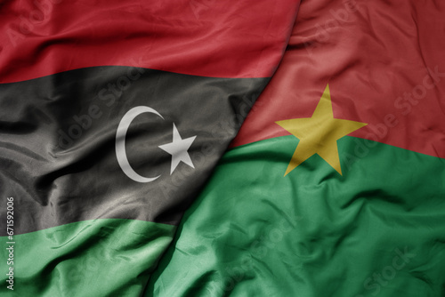big waving national colorful flag of libya and national flag of burkina faso .