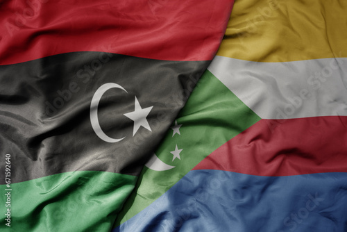 big waving national colorful flag of libya and national flag of comoros .