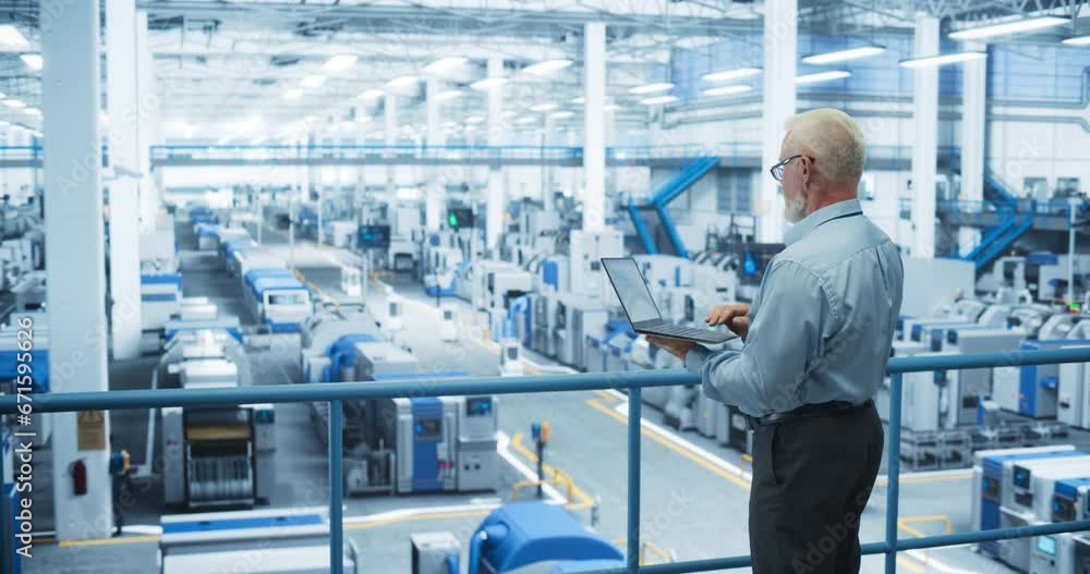 Middle Aged Male Engineer Standing on a Platform, Using Laptop Computer and Monitoring Production at a Modern Automated Electronics Manufacture with AI Robots. Factory Technician at Work Middle Aged Male Engineer Standing on a Platform, Using Laptop Computer and Monitoring Production at a Modern Automated Electronics Manufacture with AI Robots. Factory Technician at Work