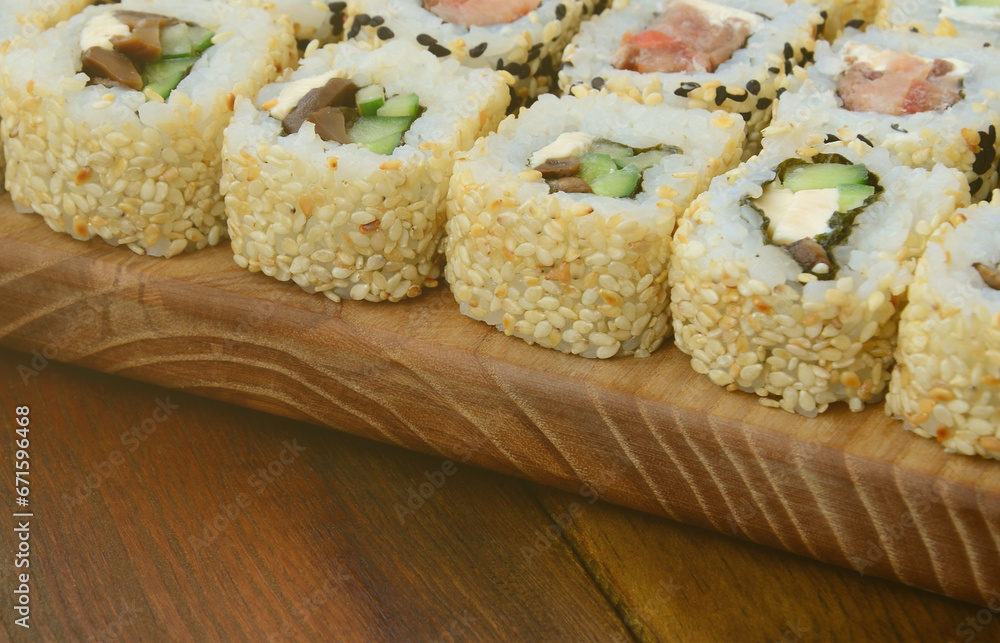 Close-up of a lot of sushi rolls with different fillings lie on a wooden surface. Macro shot of cooked classic Japanese food with a copy space. Close-up of a lot of sushi rolls with different fillings lie on a wooden surface. Macro shot of cooked classic Japanese food with a copy space.