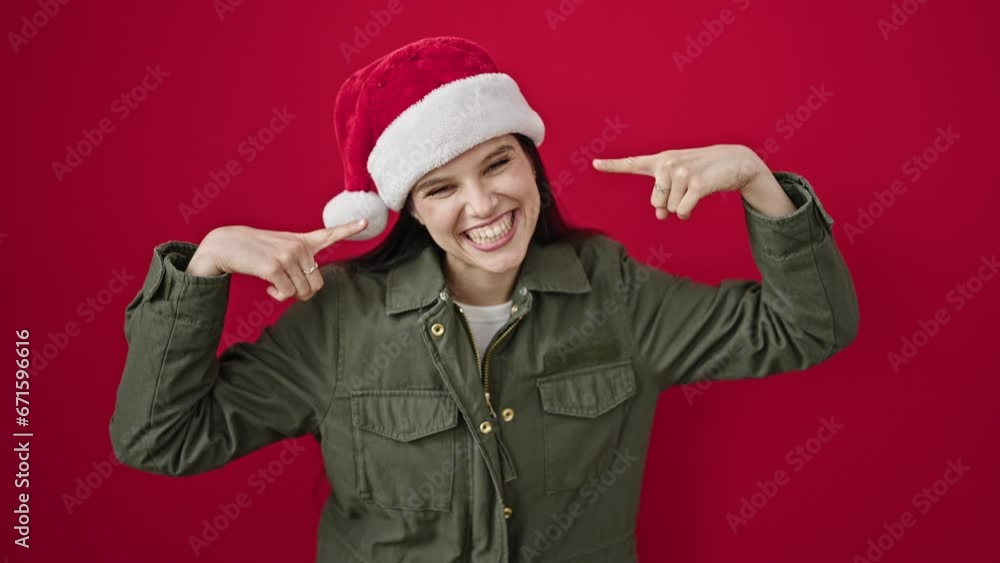 Young beautiful hispanic woman smiling confident pointing to christmas hat over isolated red background Young beautiful hispanic woman smiling confident pointing to christmas hat over isolated red background