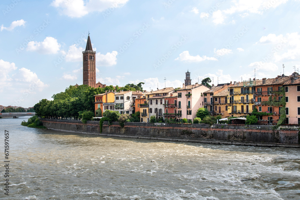 View from Ponte Pietra bridge Verona, Italy towards ancient houses along embankment of Adige River with gothic style church Chiesa di Sant'Anastasia or Basilica of Saint Anastasia in background