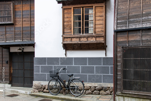 Urban street view of façade of typical Japanese house with modern stone and traditional wooden window and door features and bicycle parked in front of building