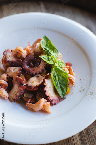 Grilled octopus cooked with spicy sauce and basil on a white plate