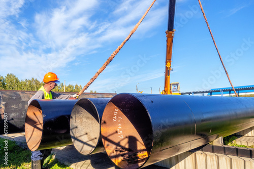 Slinger unloads large gasification pipes on summer day. Pipes for transporting natural gas. Construction of gas pipeline. Storage of large diameter metal pipes. photo