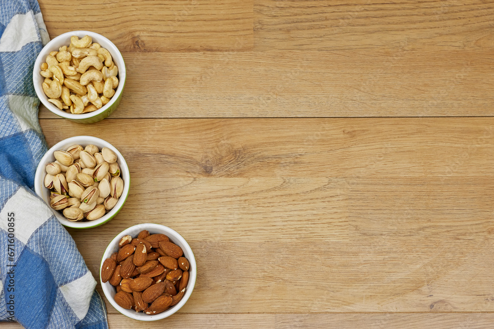 nuts (almonds, pistachio, cashews) in bowls on wooden table