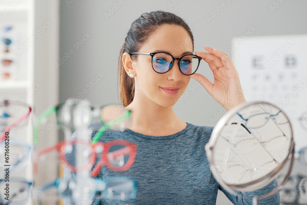 Young smiling woman choosing her new glasses - obrazy, fototapety, plakaty 