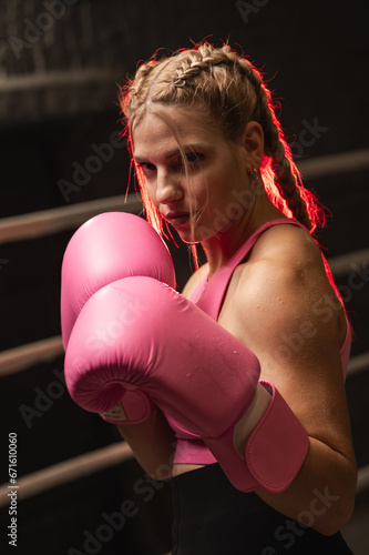 Sporty fighter girl in pink boxing gloves training or posing in the ring