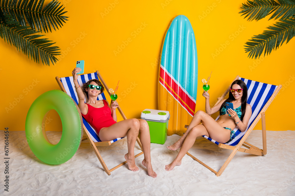 Photo of two girls sit deckchair chill rest relax in exotic tropics resort using cell phones for selfi blog post isolated bright color background