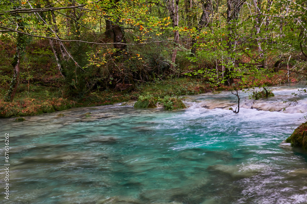Obraz premium The waterfalls and crystal clear, blue, turquoise and green waters of the Nacedero del Urederra, with its beech forest with its autumn colors in the Sierra de Urbasa-Andía. Navarre. Spain
