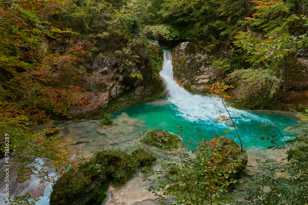 Naklejka premium The waterfalls and crystal clear, blue, turquoise and green waters of the Nacedero del Urederra, with its beech forest with its autumn colors in the Sierra de Urbasa-Andía. Navarre. Spain