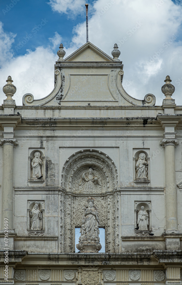 Guatemala, La Antigua - July 20, 2023: Closeup of free standing white front facade top with 6 statues of Mary, God himself, apostles, and saints under blue cloudscape