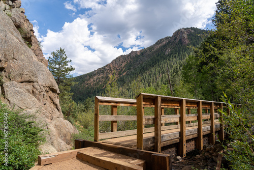 A bridge on the Seven Bridges Trail in North Cheyenne Cañon Park in Colorado Springs, CO in the late afternoon on a sunny summer day, with trees, red rocks, and mountains in the landscape