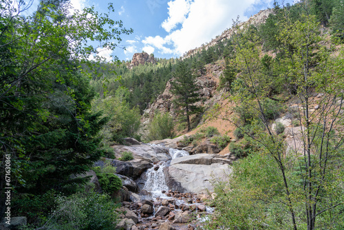 A waterfall cascade on the Seven Bridges Trail in North Cheyenne Cañon Park in Colorado Springs, CO in the late afternoon on a sunny summer day, with trees, red rocks, and mountains in the landscape