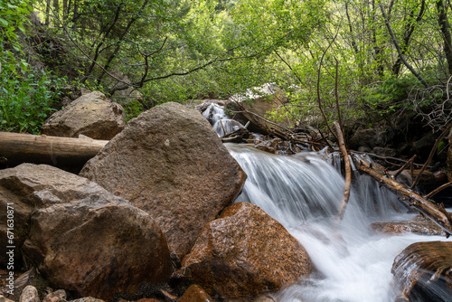 A waterfall cascade on the Seven Bridges Trail in North Cheyenne Cañon Park in Colorado Springs, CO in the late afternoon on a sunny summer day, with trees, red rocks, and mountains in the landscape
