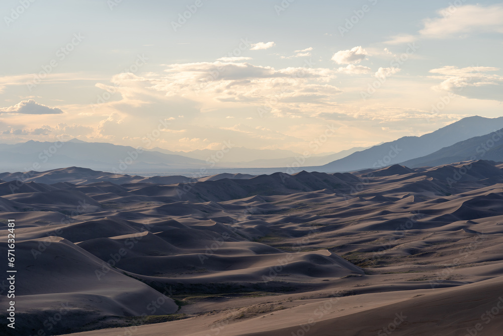Naklejka premium View from the top at golden hour and sunset at Great Sand Dunes National Park in Colorado on a sunny summer evening, with mountains in the background