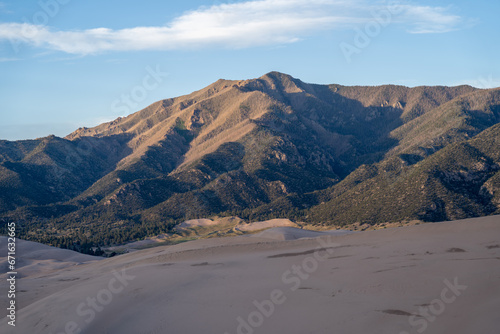 View from the top at golden hour and sunset at Great Sand Dunes National Park in Colorado on a sunny summer evening  with mountains in the background