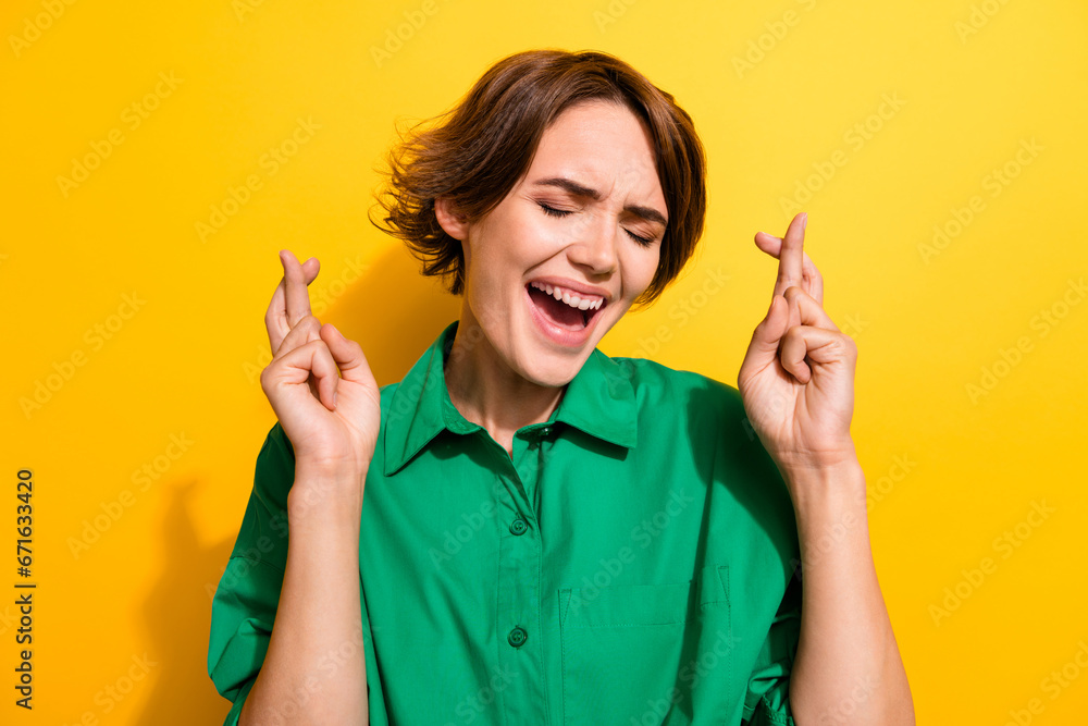 Photo of terrified horrified lady wear green shirt closed eyes fingers crossed isolated yellow color background