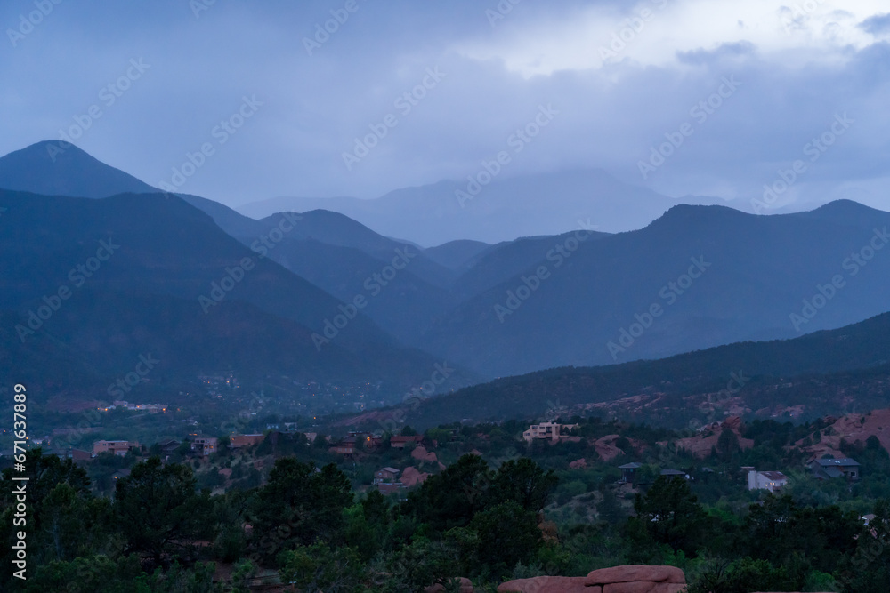 Fototapeta premium A view of a rainstorm over Pike's Peak and other blue misty mountains on a cloudy summer evening, as viewed from Garden of the Gods in Colorado Springs, CO