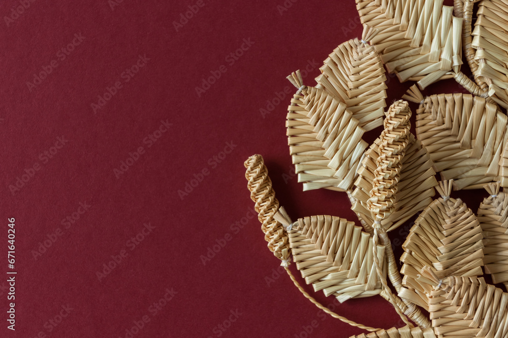 Obraz premium The branch with leaves is made of straw. Straw wall decoration. The products are made of straw. Decoration of straw on a red background