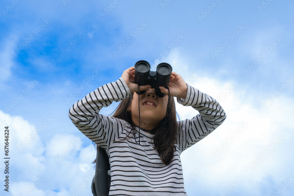 Obraz premium Cute little girl with binoculars on the mountain on a sunny day. Young girl uses binoculars when going hiking. Active young girl uses binoculars on a trip and smiles happily.