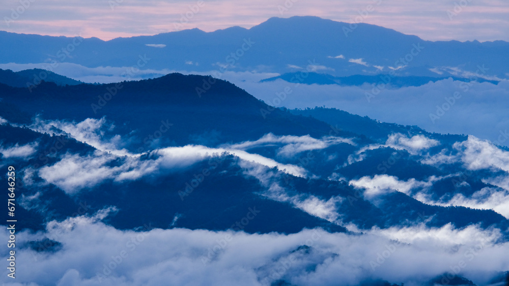 Aerial view over the mountains with sea of fog during morning sunrise in blue sky. Sea of clouds around mountain peaks at sunrise. Unseen travel in Northern Thailand. Aerial view over the mountains with sea of fog during morning sunrise in blue sky. Sea of clouds around mountain peaks at sunrise. Unseen travel in Northern Thailand.